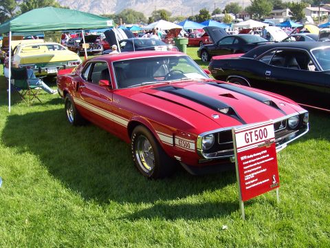 1973 Ford Mustang - A red 1970 Shelby Mustang GT500 is displayed at a car show with other vehicles in the background.