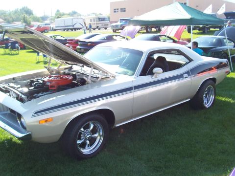 1973 Ford Mustang - A gold 1970 Plymouth Barracuda with its hood open is parked on grass at an outdoor car show.