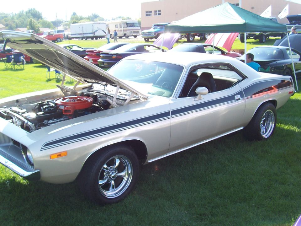Gold 1970 Plymouth Barracuda with black racing stripes, hood open, on display