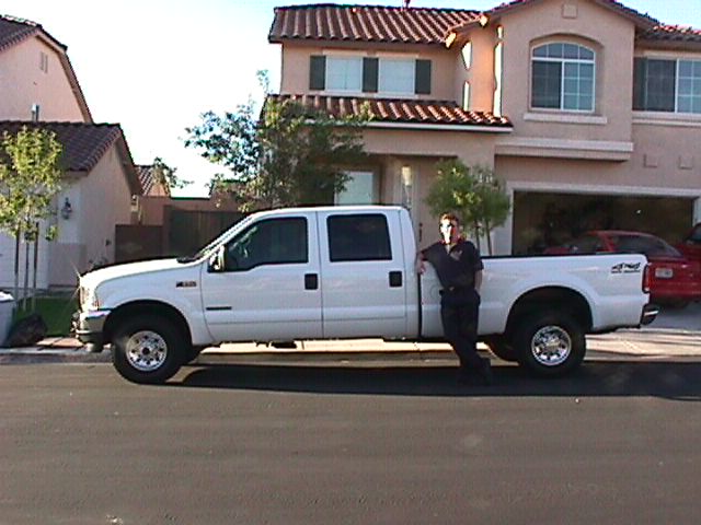 White Ford F-series 4x4 crew cab pickup with person standing beside it in front of two-story home
