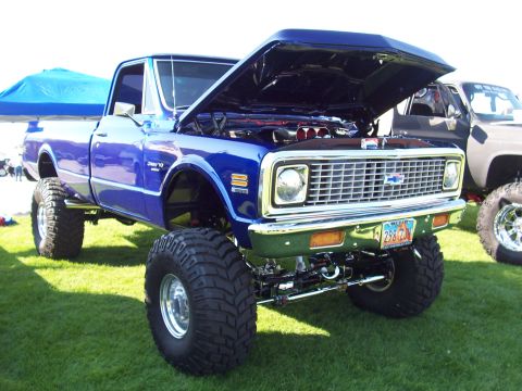 1973 Ford Mustang - A lifted blue pickup truck with its hood open is displayed on a grassy field, with another truck visible in the background.