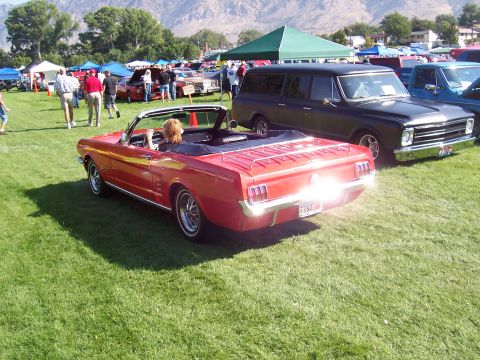 1973 Ford Mustang - A red convertible is parked on a grassy field during a car show, with other vehicles and tents in the background.