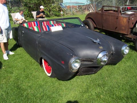 1973 Ford Mustang - A custom black convertible with a vibrant striped interior sits on display next to a rusty hot rod.
