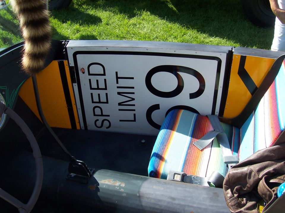 Car interior with a 'SPEED LIMIT 65' sign mounted behind the seats and a striped seat cover