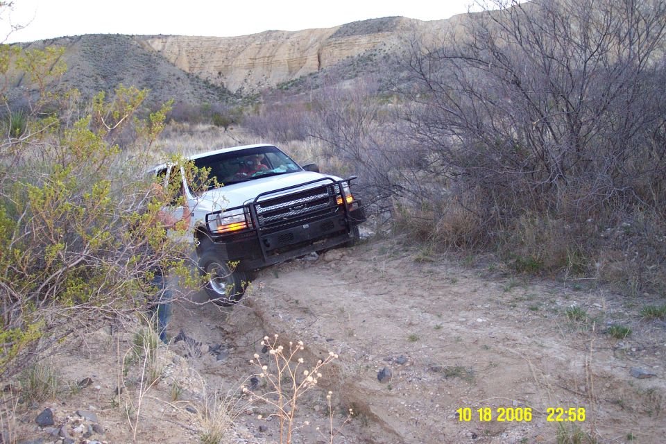 White Ford Excursion with grille guard off-roading down a rutted dirt wash in desert terrain