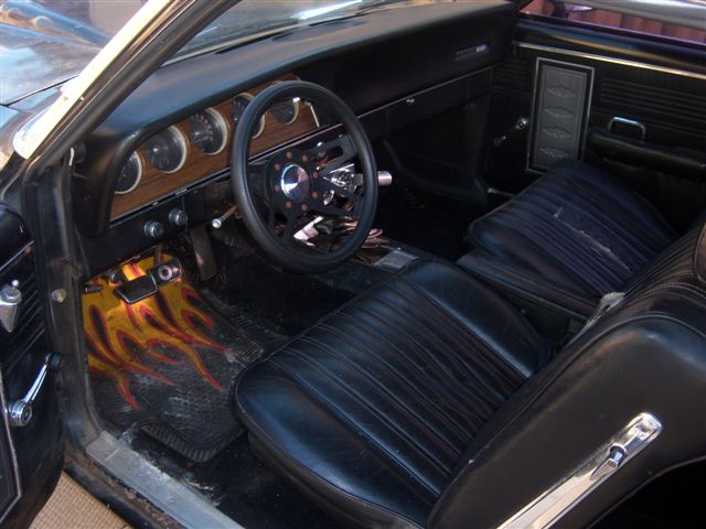 Classic car interior with black seats, sport steering wheel, and flame-print floor mat