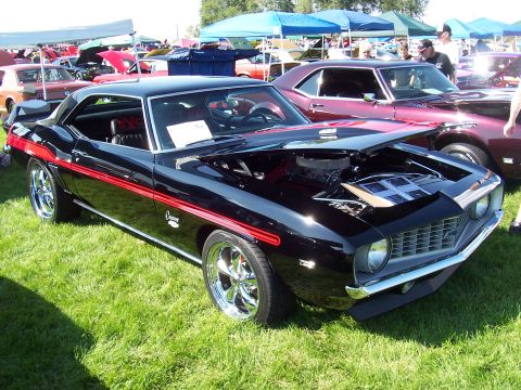 1973 Ford Mustang - A black Chevrolet Camaro with red racing stripes is displayed with its hood open at an outdoor car show.