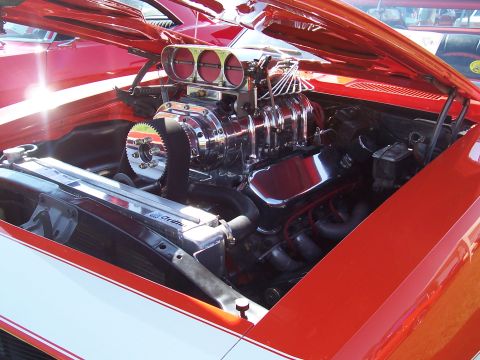 1973 Ford Mustang - The engine bay of a red car features a prominent chrome supercharger with triple carburetors.