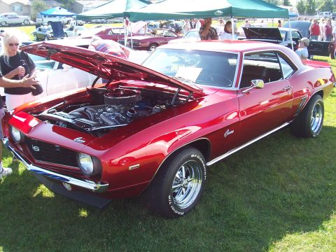 1973 Ford Mustang - A shiny red 1969 Chevrolet Camaro SS is displayed with its hood up at a car show, revealing the engine bay.