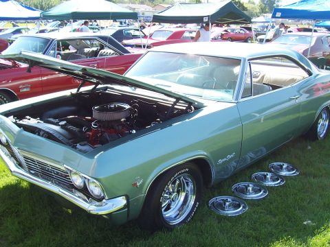 1973 Ford Mustang - A light green 1965 Chevrolet Impala coupe is displayed with its hood open at an outdoor car show.