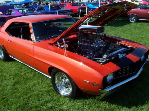 1973 Ford Mustang - Orange 1969 Camaro Z/28 at a car show, a prominent supercharged engine under the open hood.