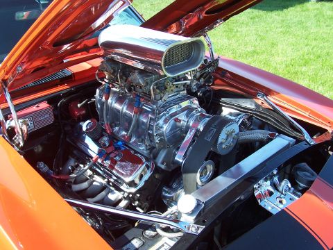 1973 Ford Mustang - The engine bay of an orange car features a prominent chrome supercharger with a large air intake scoop.