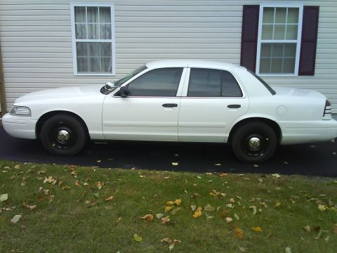 2003 Ford Crown Victoria - Side profile of a white 2003 Ford Crown Victoria, showing its full body and black steel wheels.