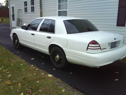 2003 Ford Crown Victoria - A white 2003 Ford Crown Victoria sedan is parked on a driveway next to a house.