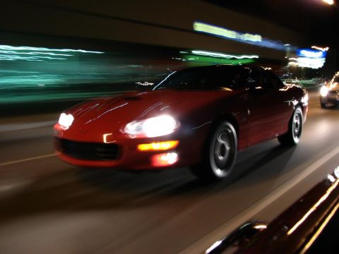 2003 Ford Crown Victoria - A red sports car speeds down a highway at night, with motion blur indicating high speed.