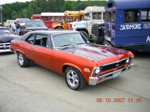 1972 Ford Ranchero - This orange muscle car, likely a 1970s Chevrolet Nova SS, is parked in front of several buses.