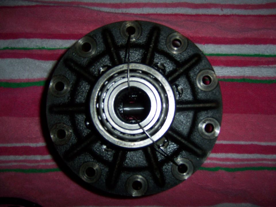 Close-up of a differential carrier with a bearing installed. It has a black, cast-iron housing with ten bolt holes around the perimeter