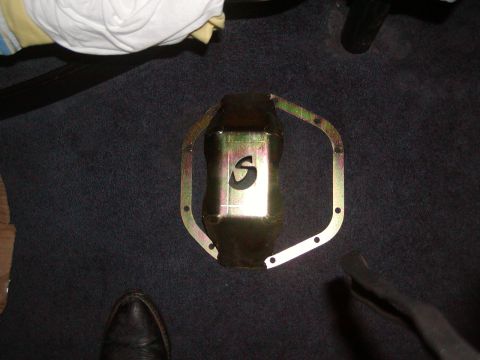 1991 Ford Bronco - A gold-colored oil pan with a black 'S' cutout and a metal gasket is shown on a dark carpeted surface.
