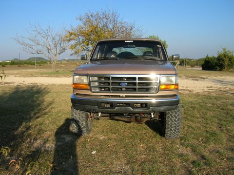 1996 Ford Bronco - A lifted brown Ford Bronco is parked on a grassy area under a clear blue sky.