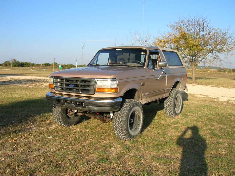 Lifted tan Ford Bronco front three-quarter view on grass with mud-terrain tires