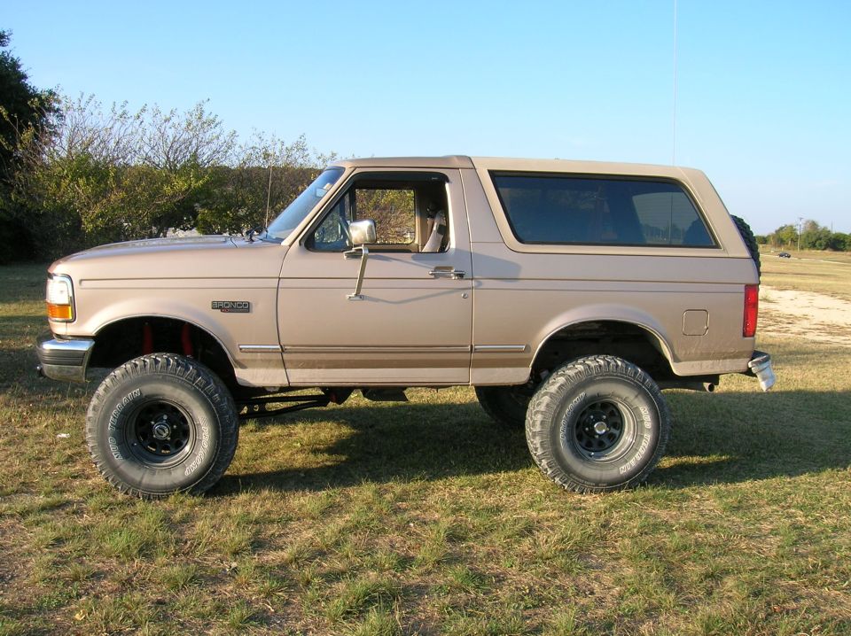 Lifted tan Ford Bronco side profile on grass with mud-terrain tires and black steel wheels