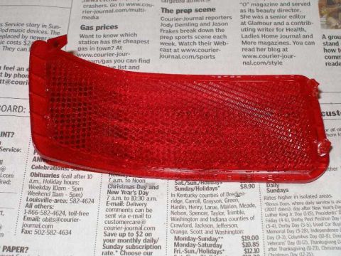 2001 Ford Crown Victoria - A red reflector part is shown against a newspaper background.