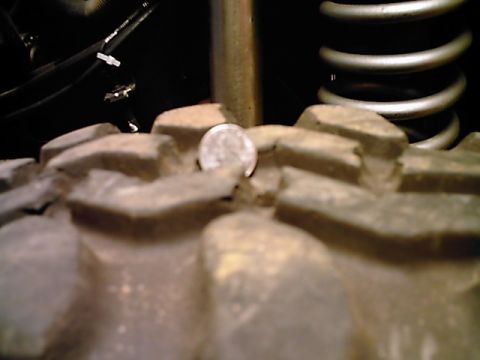 1995 Ford Bronco - A coin is lodged in the aggressive tread of a large off-road tire, with a suspension spring visible.