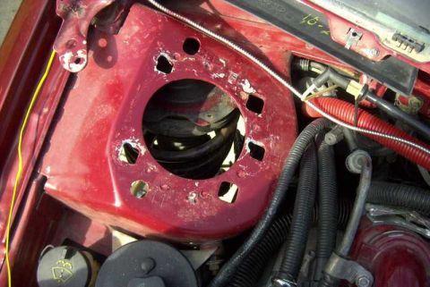 1997 Ford Taurus - Top-down view into a dark red strut tower in an engine bay with the strut mount removed, exposing the coil spring down inside the opening.…