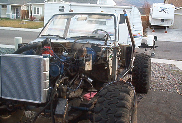 Front end of a vehicle being worked on, with engine exposed and large tires