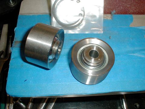 1996 Ford Bronco - Two suspension rollers and a C-clip are laid out on a blue surface, possibly for repair or replacement.