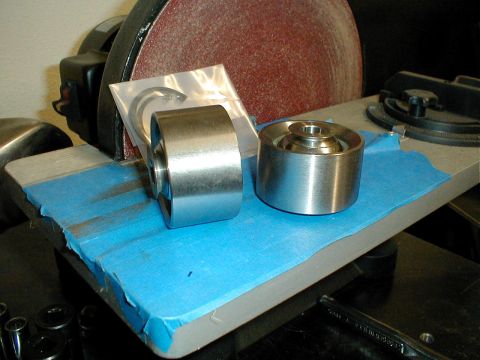 1996 Ford Bronco - Two metal pulleys and a c-clip are placed on blue tape in front of a belt sander.