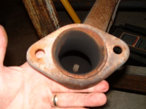 1995 Ford Bronco - A close-up view of a rusty exhaust pipe flange, held by a hand with a ring.