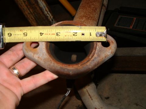 1995 Ford Bronco - A hand holds a tape measure against a rusty exhaust pipe flange, indicating its size.