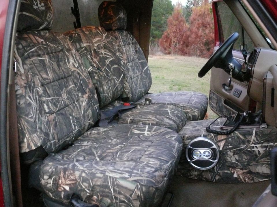 Interior view of vehicle seats covered in camouflage fabric, with a steering wheel visible