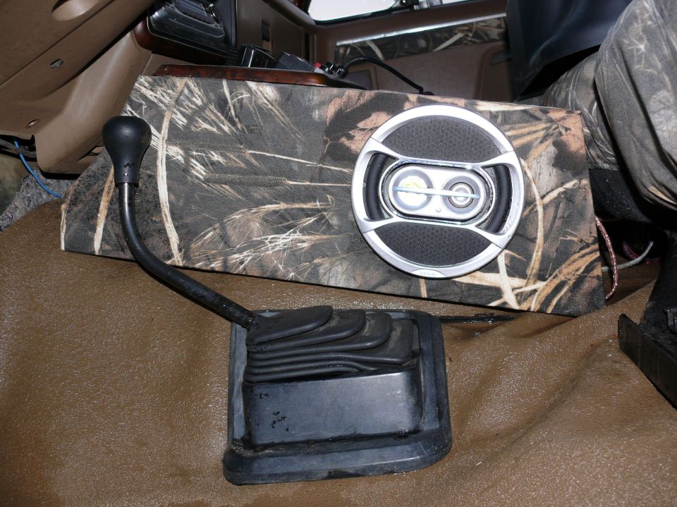 Gear shifter and camo-covered speaker box with a round speaker in a vehicle interior
