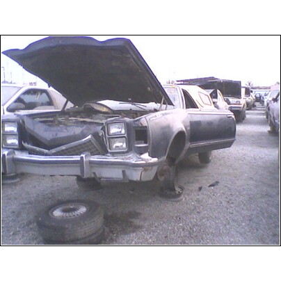 1973 Ford Ranchero - A dark-colored pickup truck sits in a junkyard with its hood open and one wheel removed.