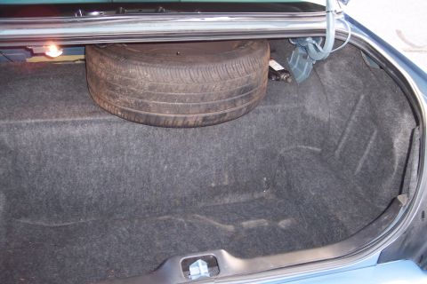 2001 Ford Crown Victoria - The interior of a car trunk shows a spare tire and a jack, with the trunk light illuminated.