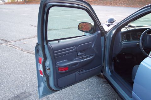 2001 Ford Crown Victoria - Interior view of a blue police car with the driver's door ajar, revealing the dashboard and door panel.