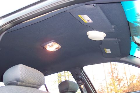2001 Ford Crown Victoria - Interior shot of a vehicle's headliner, showing the dome light and sun visors. A warning label is visible on the passenger-side visor.