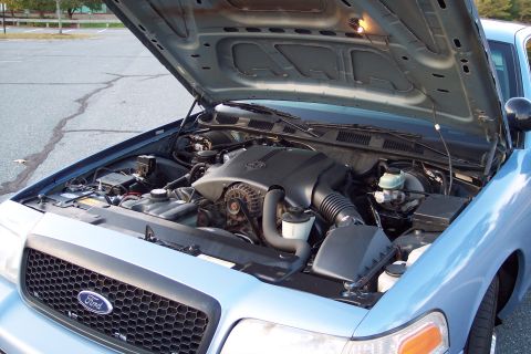 2001 Ford Crown Victoria - The engine bay of a light blue Ford Crown Victoria is shown with the hood open, revealing the engine and surrounding components.