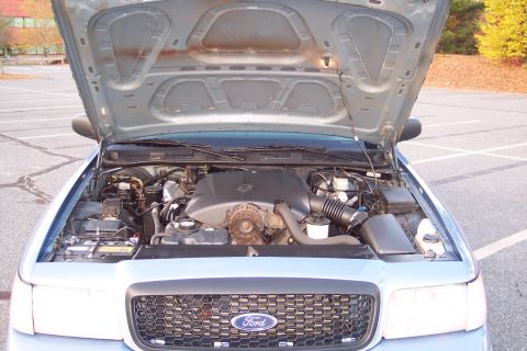 2001 Ford Crown Victoria - The engine bay of a 2001 Ford Crown Victoria is visible with the hood open, revealing the engine and front grille.