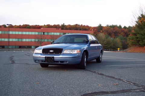 2001 Ford Crown Victoria - A blue Ford Crown Victoria is parked in a lot during autumn, with fall foliage visible on the trees.