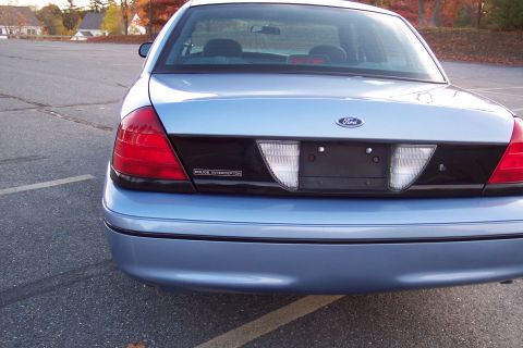 2001 Ford Crown Victoria - The rear of a light blue 2001 Ford Crown Victoria Police Interceptor is shown in a parking lot with autumn trees in the background.