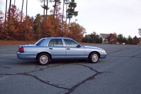 2001 Ford Crown Victoria - A light blue 2001 Ford Crown Victoria sedan is seen from the side in a parking lot with autumn trees in the background.