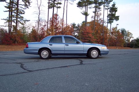 2001 Ford Crown Victoria - Side view of a blue 2001 Ford Crown Victoria sedan in a parking lot during autumn.
