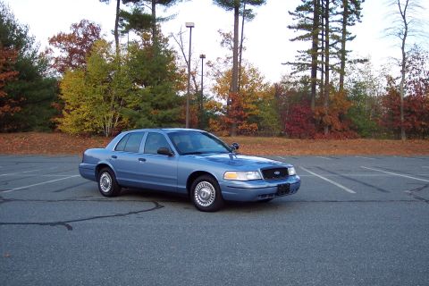 2001 Ford Crown Victoria - A blue sedan is parked in a lot during autumn, with trees showing fall colors.