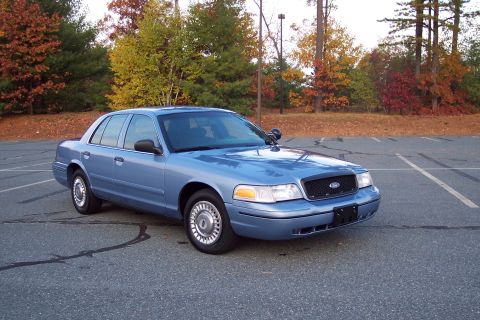2001 Ford Crown Victoria - A blue 2001 Ford Crown Victoria is parked in an asphalt lot with fall foliage visible behind it.