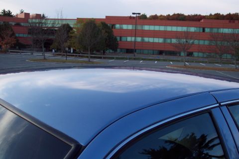 2001 Ford Crown Victoria - The reflection on the blue car's roof shows the surrounding environment, including a large red brick building.