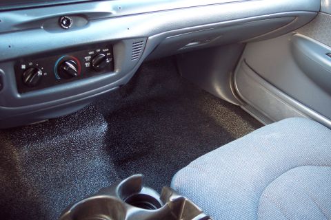2001 Ford Crown Victoria - The interior of a car features textured flooring and a dashboard with climate control knobs and vents.