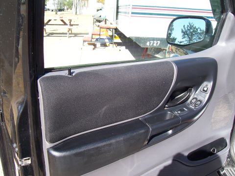 2003 Ford Ranger - Close-up of the driver's side interior door panel, showing the fabric insert and power window controls.